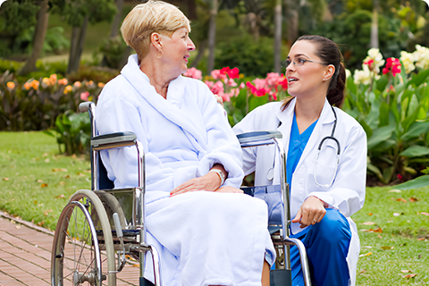 A woman in white robe sitting on a wheelchair next to a nurse.